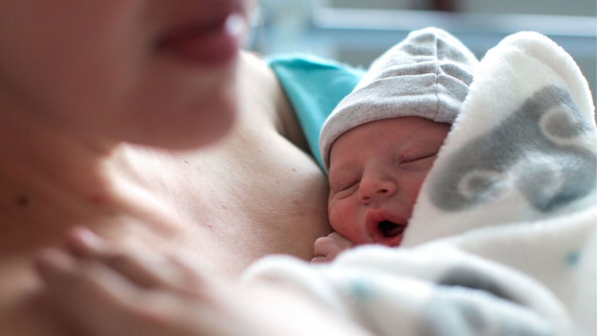 newborn wearing a tiny beanie leans against his mother