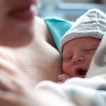 newborn wearing a tiny beanie leans against his mother