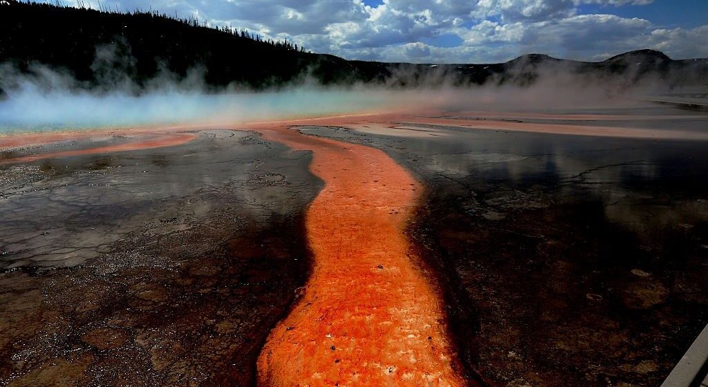 A picture of Midway Geiser in Yellowstone National Park shows streams of red liquid flowing away from its center.