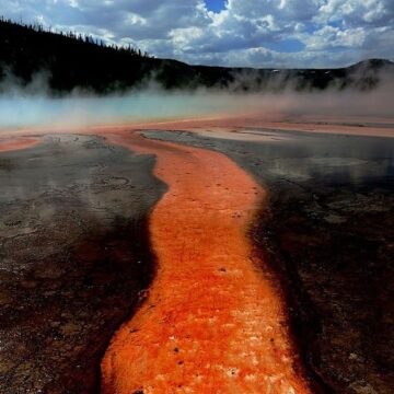 A picture of Midway Geiser in Yellowstone National Park shows streams of red liquid flowing away from its center.